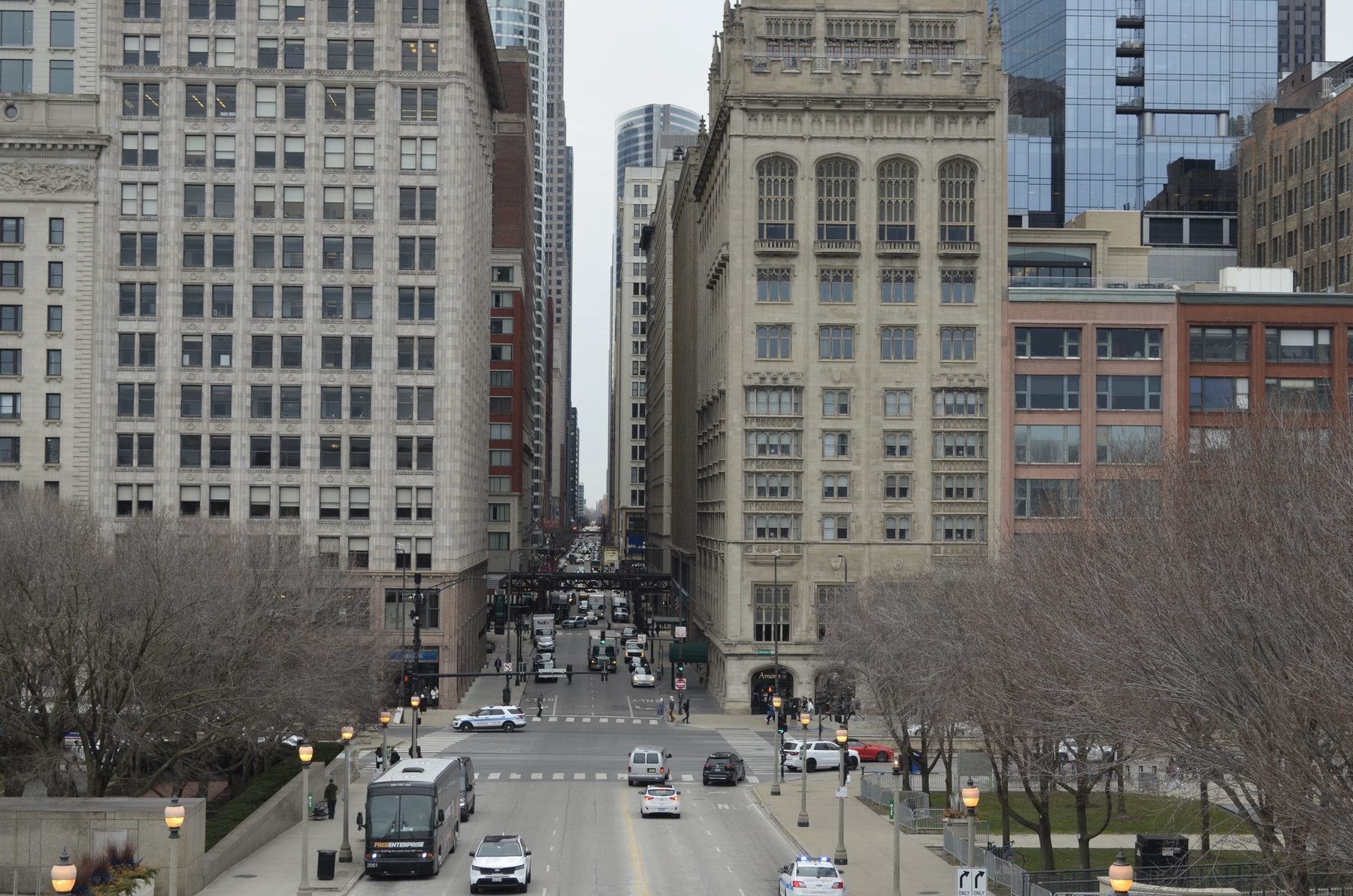 A street receding between stone and glass buildings in the Loop, with buses and police cars below