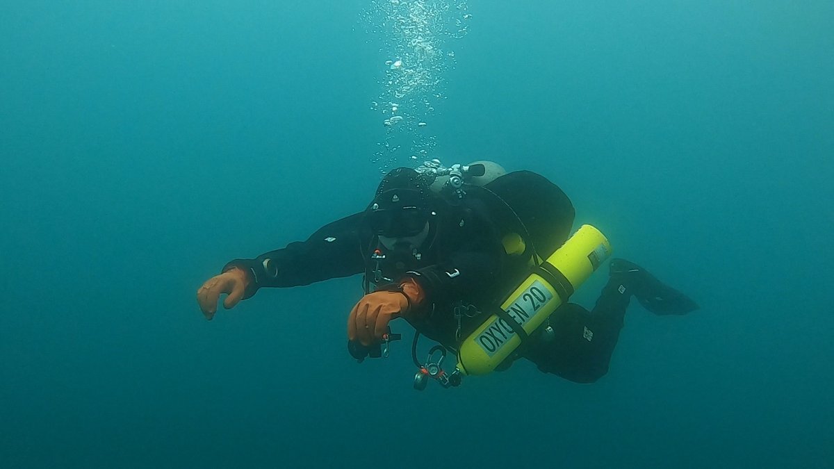 Kian scuba diving, trailing bubbles, wearing a yellow OXYGEN 20 stage tank