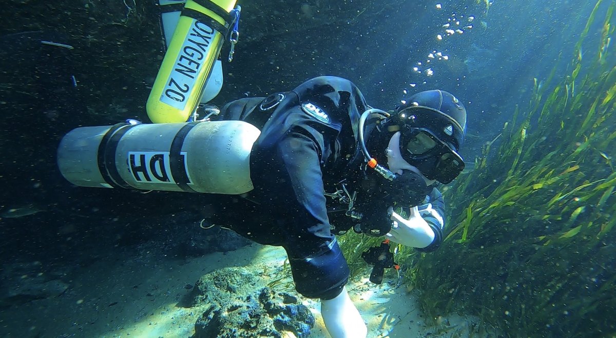 Kian scuba diving near grass and rock, stage bottle visible
