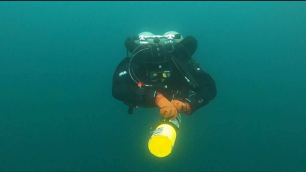 Diver holding a lit stage bottle in open water
