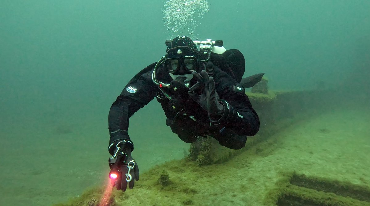 Diver giving an OK sign near a wreck in green water