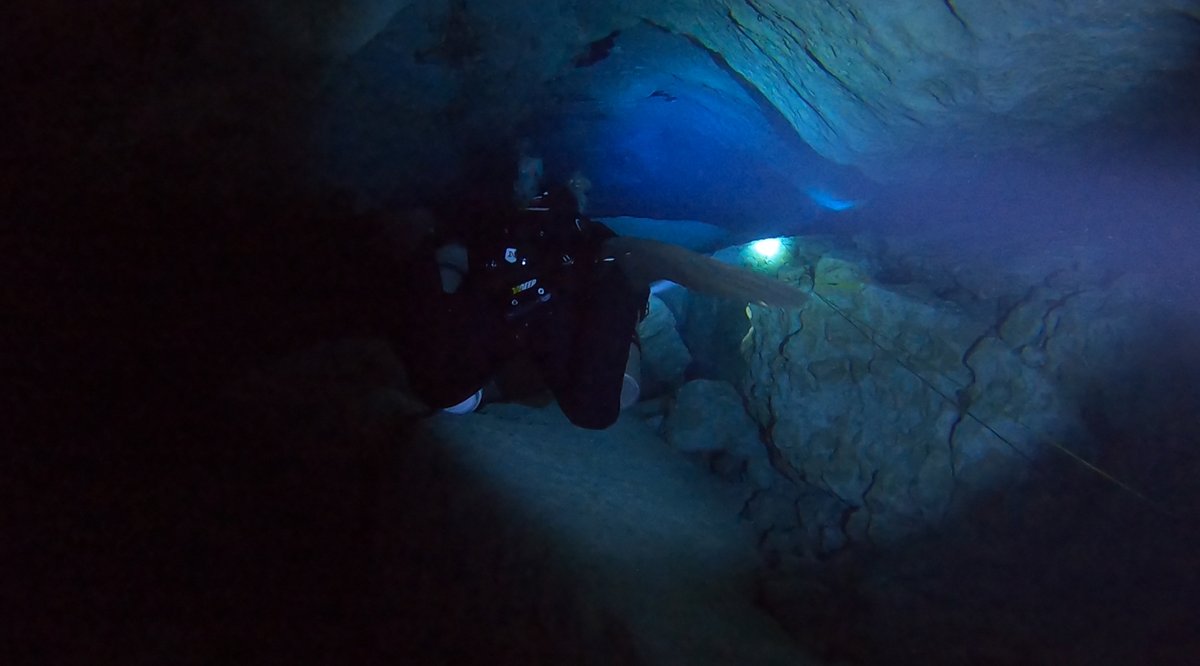 Diver in a cave approaching a distant lit opening
