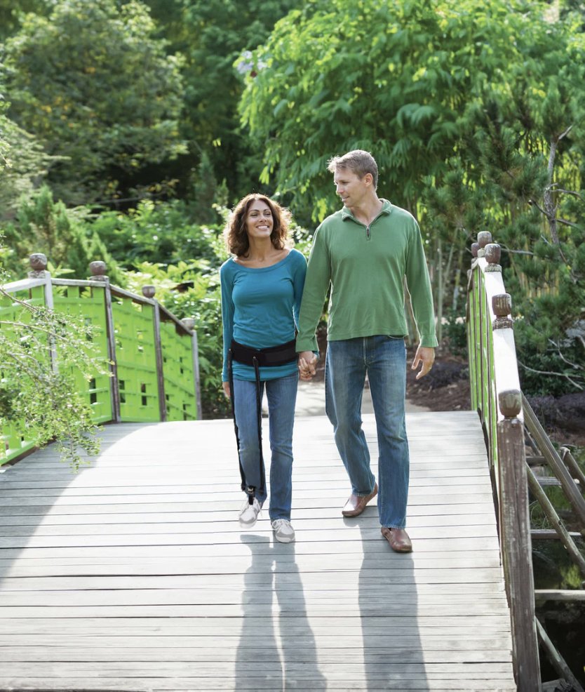 A couple walking outdoors, the woman wearing a visible external hip flexion assist brace over her clothing.